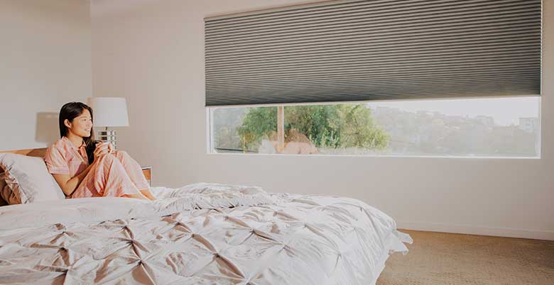 Woman enjoying coffee in bed looking at cellular shades