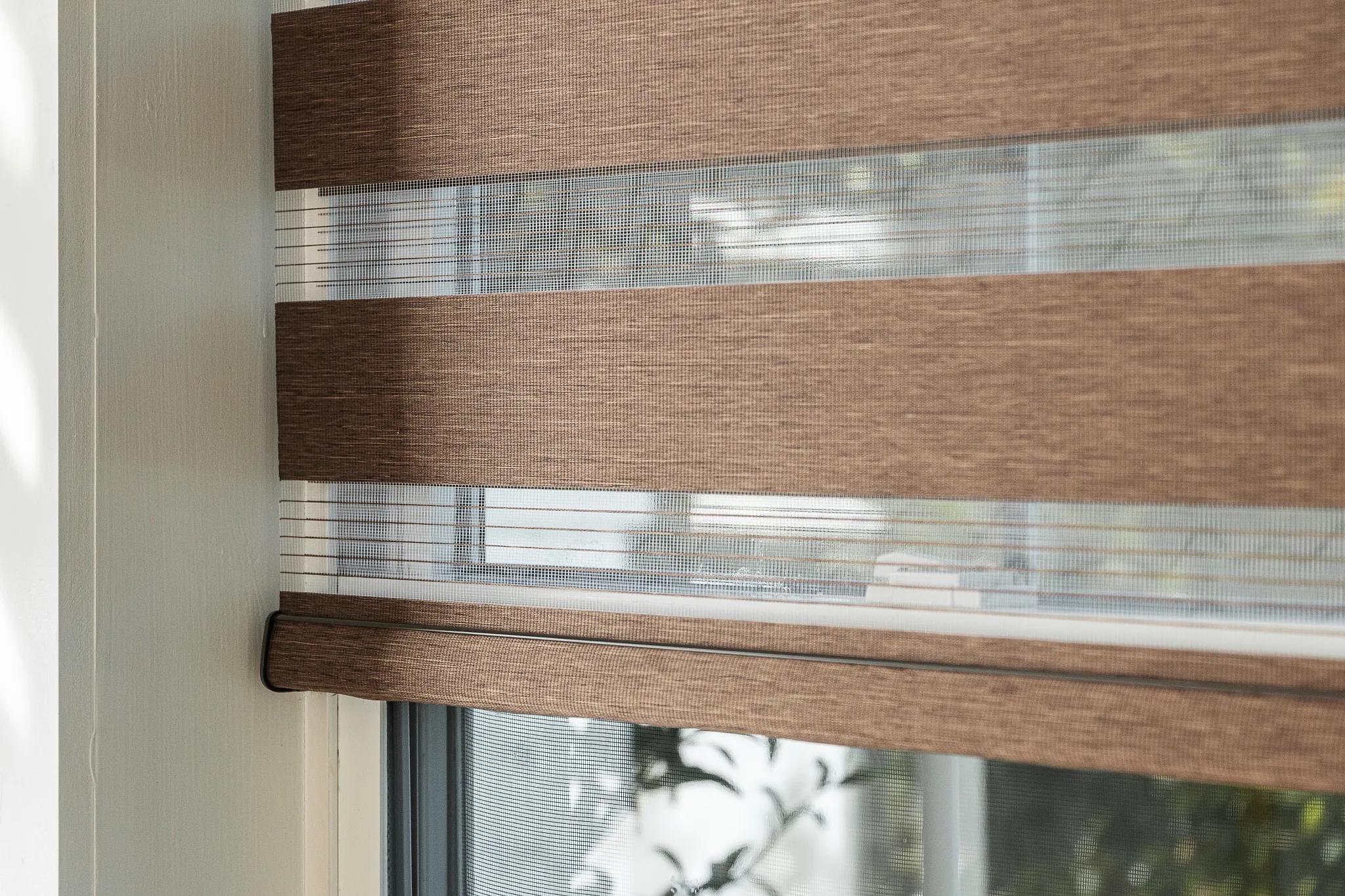 Close-up of tan zebra shades filtering sunlight and casting striped shadows on a white wall